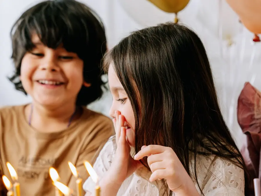 Crianças sorrindo diante de um bolo de aniversário com velas acesas