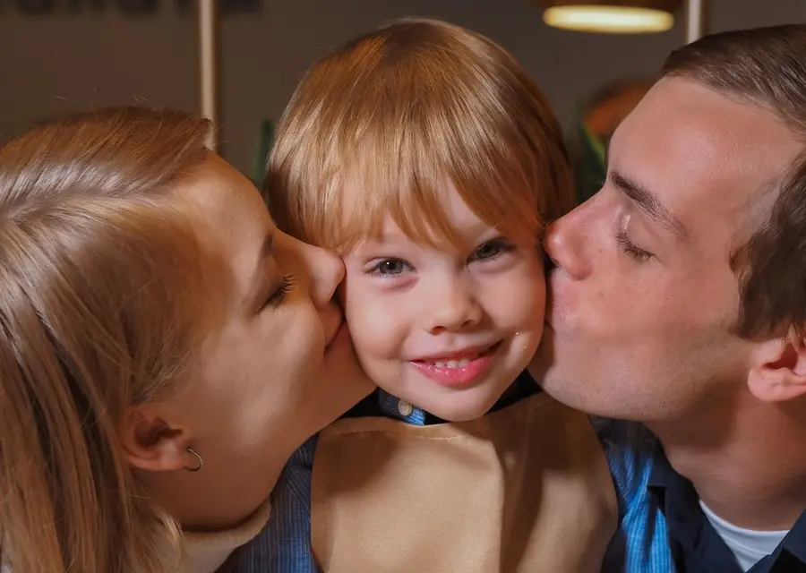 Pais beijando o filho sorridente enquanto comem pizza juntos