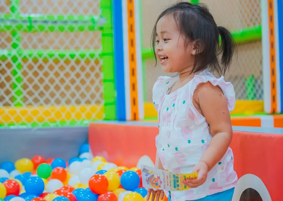 Criança sorrindo enquanto brinca na piscina de bolinhas do espaço kids