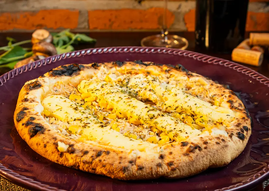 Pizza artesanal da casa em forno a lenha, servida no prato bordô